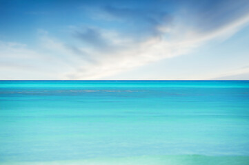 Fototapeta na wymiar Blue sea against blurry sky with soft clouds summer background