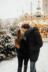 Couple near carousel on Christmas market. Young romantic couple in love walking in the city and...
