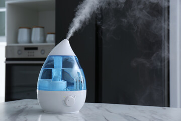 Modern air humidifier on marble table in kitchen. Space for text