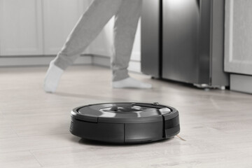 Modern robotic vacuum cleaner and blurred woman on background