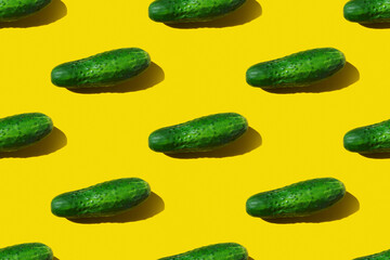 Pattern with a whole green cucumber with a hard clear shadow on a yellow background. Seamless texture