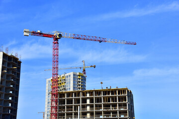 Naklejka premium Tower cranes working at construction site. Construction process of the new modern residential buildings.Tall house renovation project, government programs. Minimalistic multi storied home.