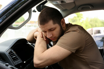 Tired man sleeping on steering wheel in his car