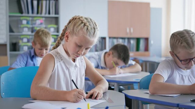 elementary school class, portrait of cute girl writes in exercise notebook, teacher checks work to the pupil during an lesson