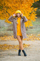 Beautiful woman walking outdoors in autumn. Smiling woman collects yellow leaves in autumn. Young woman enjoying autumn weather.