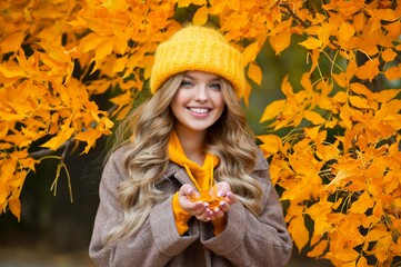 Beautiful woman walking outdoors in autumn. Smiling woman collects yellow leaves in autumn. Young woman enjoying autumn weather.