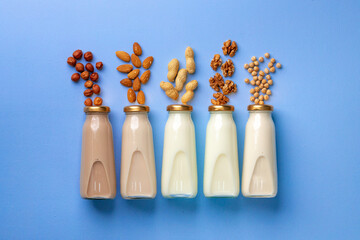 Bottles of vegan non dairy milk with various nuts on blue background