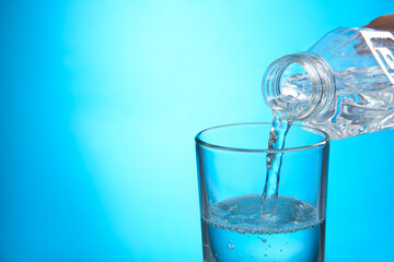 Pouring water from bottle into glass on blue background. Space for text