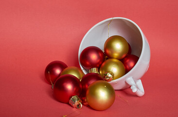 Red and gold Christmas balls lie in a white ceramic mug
