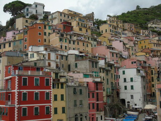 Fototapeta na wymiar Riomaggiore, Italy - 08/31/2020: Beautiful photography of the countryside from Cinque Terre, Italy. Grey sky, colourful houses, grape coltivation from the mountains, and some small waves from the sea.