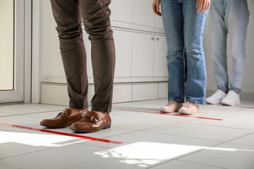 People standing in line behind taped floor markings for social distance indoors, closeup....