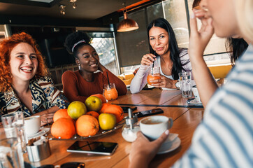 Group of young female friends having fun in cafe, talking and laughing while sitting at table.