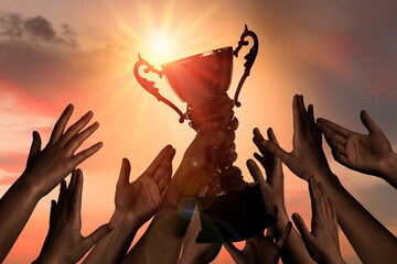 Winning team with gold trophy cup against shining sun in sky - obrazy, fototapety, plakaty