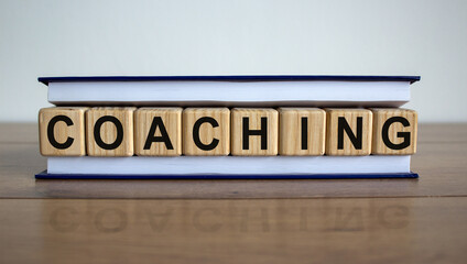 Concept word 'coaching' on wooden cubes between pages of a book on a beautiful wooden table. White background. Business concept. Copy space.