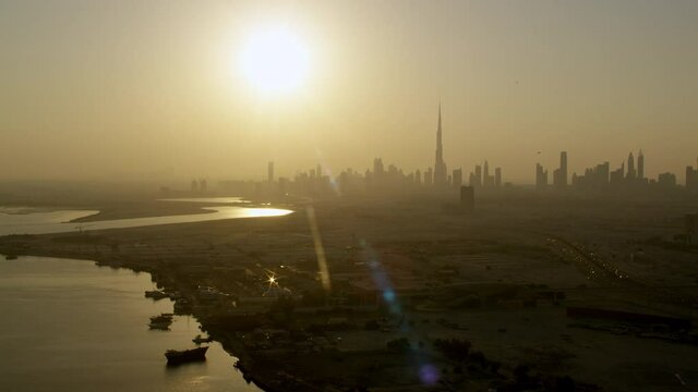 Zooming out of Al Jadaf Shipyard by the Dubai Creek to a beautiful composition with the Burj Khalifa Skyline & a glare from the sun over the city, 6-axis stabilized gimbal, Shotover F1, 8K, parallax.