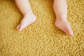 Top-down horizontal shot of little baby's feet on light brown carpet, copy space