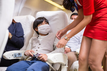 Asian boy wearing protective face mask ask for help from flight attendant or air hostess to fasten seat belt at airplane cabin. concept for travel safety and health insurance during Coronavirus