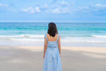 Back view of Woman in beautiful blue summer dress standing back looking to beach and sea blue sky horizon, vacation and travel ocean concept. Phuket, Thailand.