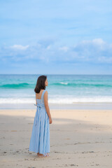 Full length of Woman in beautiful blue summer dress standing and looking to beach and sea blue sky horizon, vacation and travel ocean concept. Phuket, Thailand.