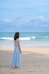 Full length of Woman in beautiful blue summer dress standing and looking to beach and sea blue sky horizon, vacation and travel ocean concept. Phuket, Thailand.