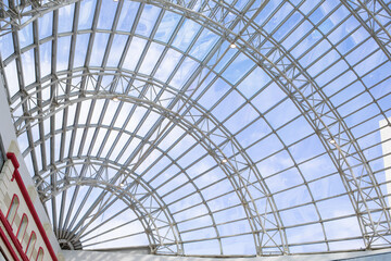 A metal structure supporting the supermarket glass dome. Transparent ceiling letting in sunlight, glass dome blue sky. Modern trendy building architecture