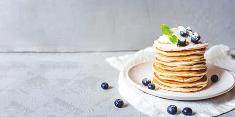 A stack of pancakes with fresh blueberries, buttercream and powdered sugar. Banner with copy space.