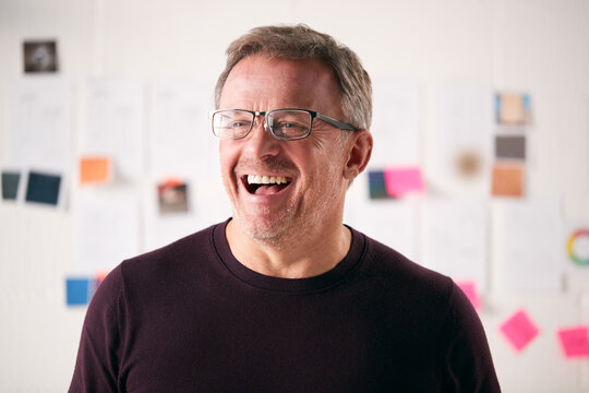 Laughing Mature Businessman Standing In Front Of Desk In Start Up Creative Business