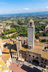 Fototapeta na wymiar Aerial view of the medieval houses, central square and towers of San Gimignano, Italy, and the surrounding fields, forests and mountains