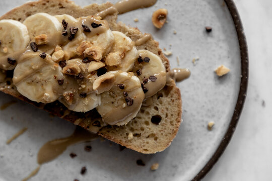 Sliced banana with tahini drizzle, hazelnuts, and cacao nibs on toast