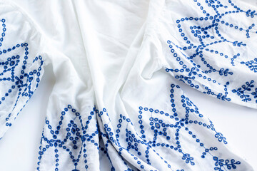 Blue embroidered on white ladies summer blouse on white surface.