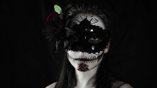 Mexican day of the dead. Young woman with sugar skull Halloween makeup looks at the camera. The woman removes the mask from her face. Happy Halloween. High quality 4k video
