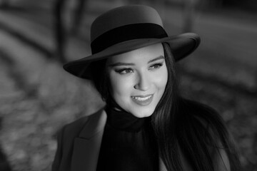 Young woman in park an autumn day. Closeup black and white portrait of charming lady in beige classic coat and hat on background of autumn leaves.