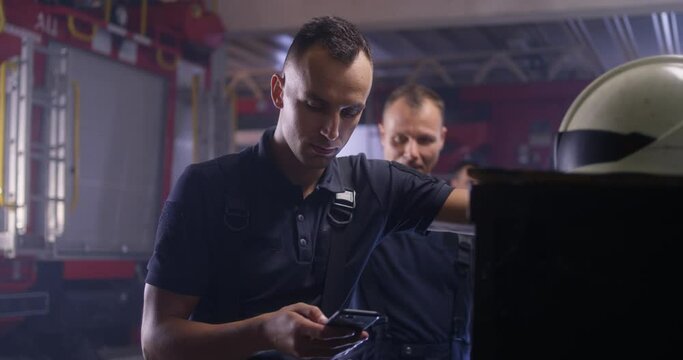 Fireman using smartphone and talking with colleague