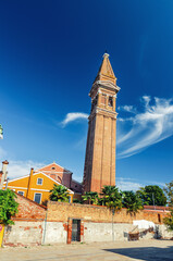 Obraz premium San Martino Roman Catholic church in Burano island with brick bell tower campanile, blue sky background in sunny summer day, Venice Province, Veneto Region, Northern Italy. Burano postcard