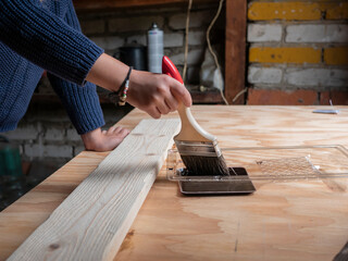 little girl paints boards in the workshop. A child's hand holds a brush for painting boards
