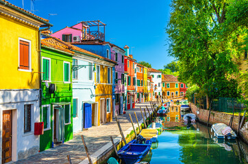 Fototapeta na wymiar Colorful houses of Burano island. Multicolored buildings on fondamenta embankment of narrow water canal with fishing boats in sunny day, Venice Province, Veneto Region, Northern Italy. Burano postcard