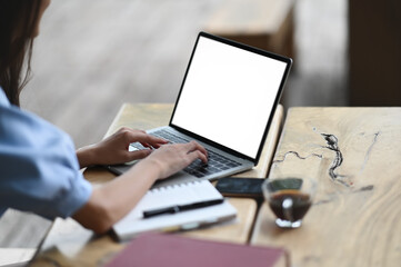 Cropped shot woman is using a white blank screen computer laptop at the wooden table.