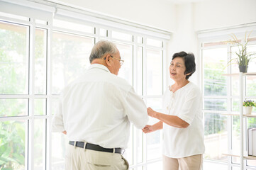 joyful senior asian retired couple is dancing and enjoying the music in the living room at home, health concept