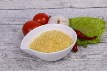 Raw couscous in the bowl served salad leaves, tomato and pepper
