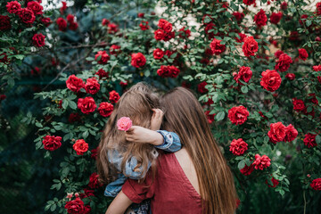 Naklejka premium upset daughter in her mother's arms is hiding from society and is looking for support in the park near red roses.