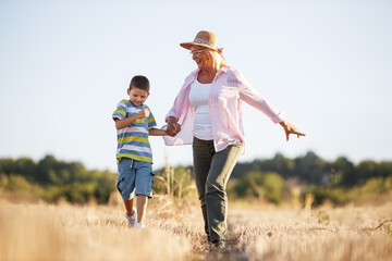 Grandmother walking on meadow with her grandson. Relaxing and joying in sunset.