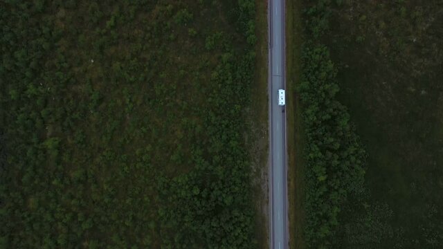 Aerial view following a camper driving on a asphalt road, in arctic nature, dark, moody, summer day, in Enontekio, Lapland, Finland - Top down, drone shot