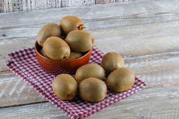 Fresh kiwi in a bowl on wooden and picnic cloth background. high angle view.