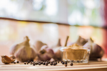 A beautiful and large garlic lies with peppercorns and garlic seasoning on a brown wooden board.