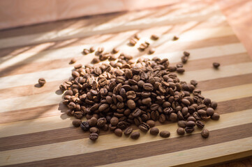 Roasted arabica coffee beans are scattered on a wooden plank.
