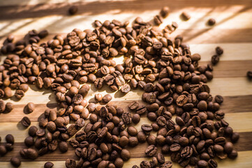 Roasted arabica coffee beans are scattered on a wooden plank.