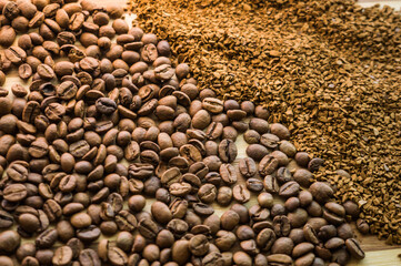 Roasted arabica coffee beans and instant coffee are scattered on a wooden board close-up.