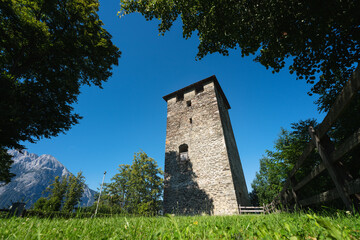 Fototapeta na wymiar The tower castle ruin of Hoertenberg between evergreen trees and rocky mountainrange, Pfaffenhofen, Tirol, Austria