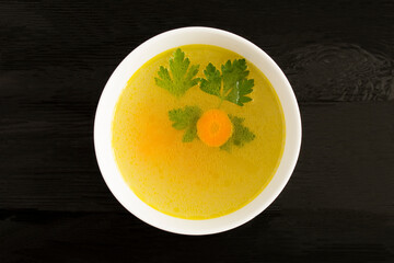 Top view of chicken broth in the white bowl on the black  surface