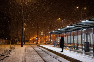young adult woman alone at tram station waiting for transport snowing winter night